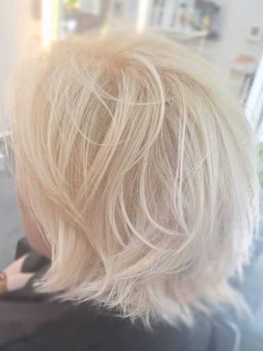 Corte bob corto a capas con coloración en rubio claro irisado sobre cabello blanco natural, con acabado luminoso y tonos perlados.